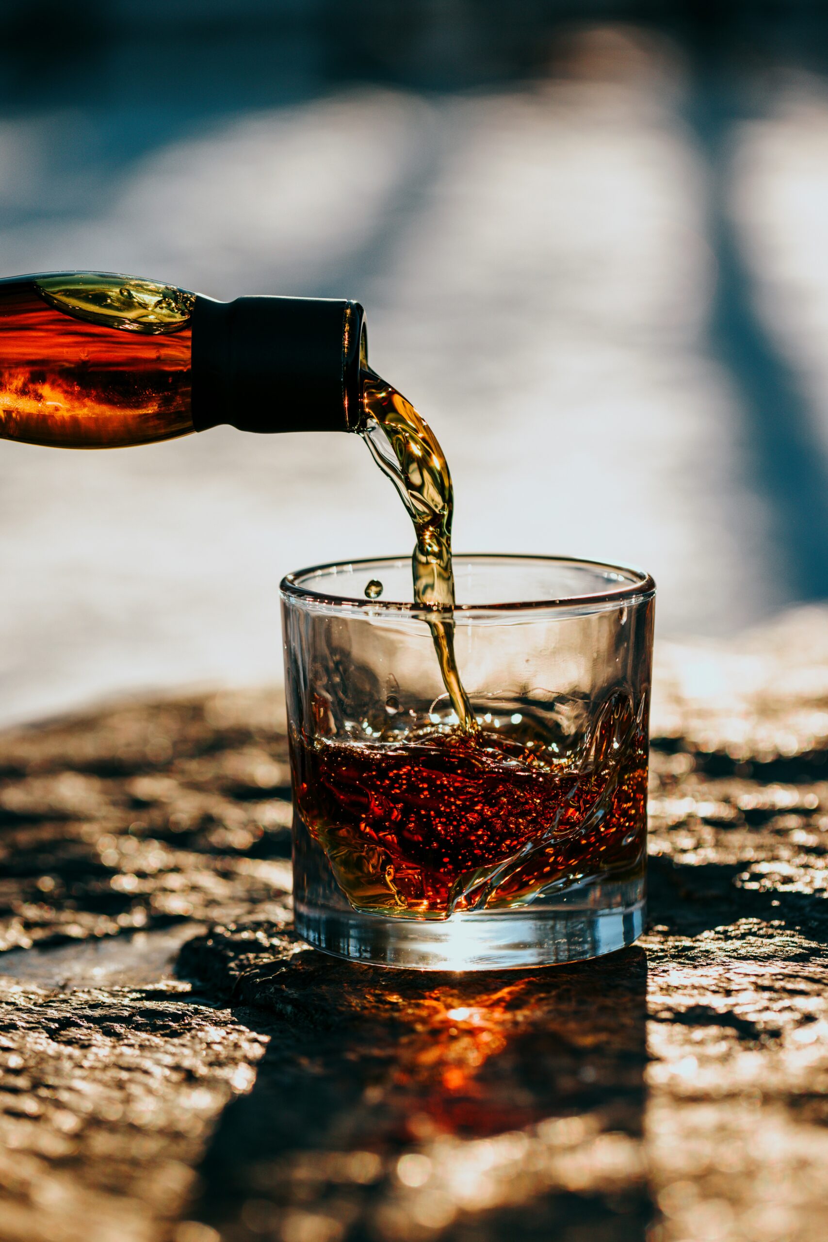 Rum poured from a bottle into a glass in sunlight